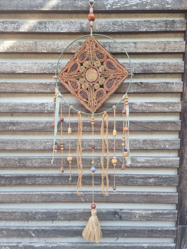Attrape-rêves motif soleil en raffia avec centre jaune sur cerclage en acier vert, perles en céramique et plumes