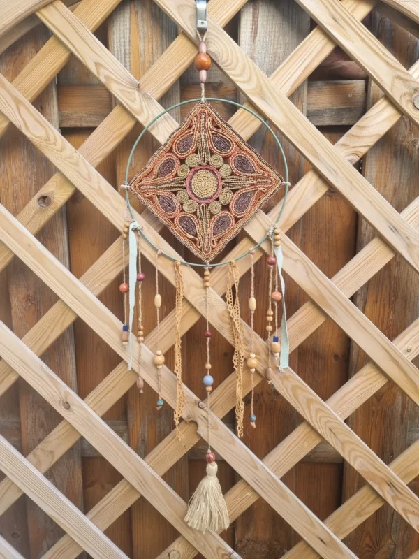 Attrape-rêves motif soleil en raffia avec centre jaune sur cerclage en acier vert, perles en céramique et plumes